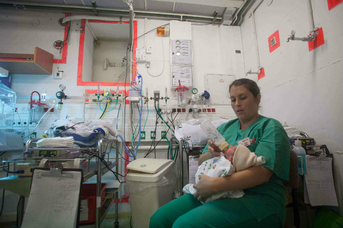 A nurse cares for a newborn in a shelter at Barzilai as a warning siren sounds for possible incoming rockets in Asheklon. Photo by Uri Lenz/FLASH90