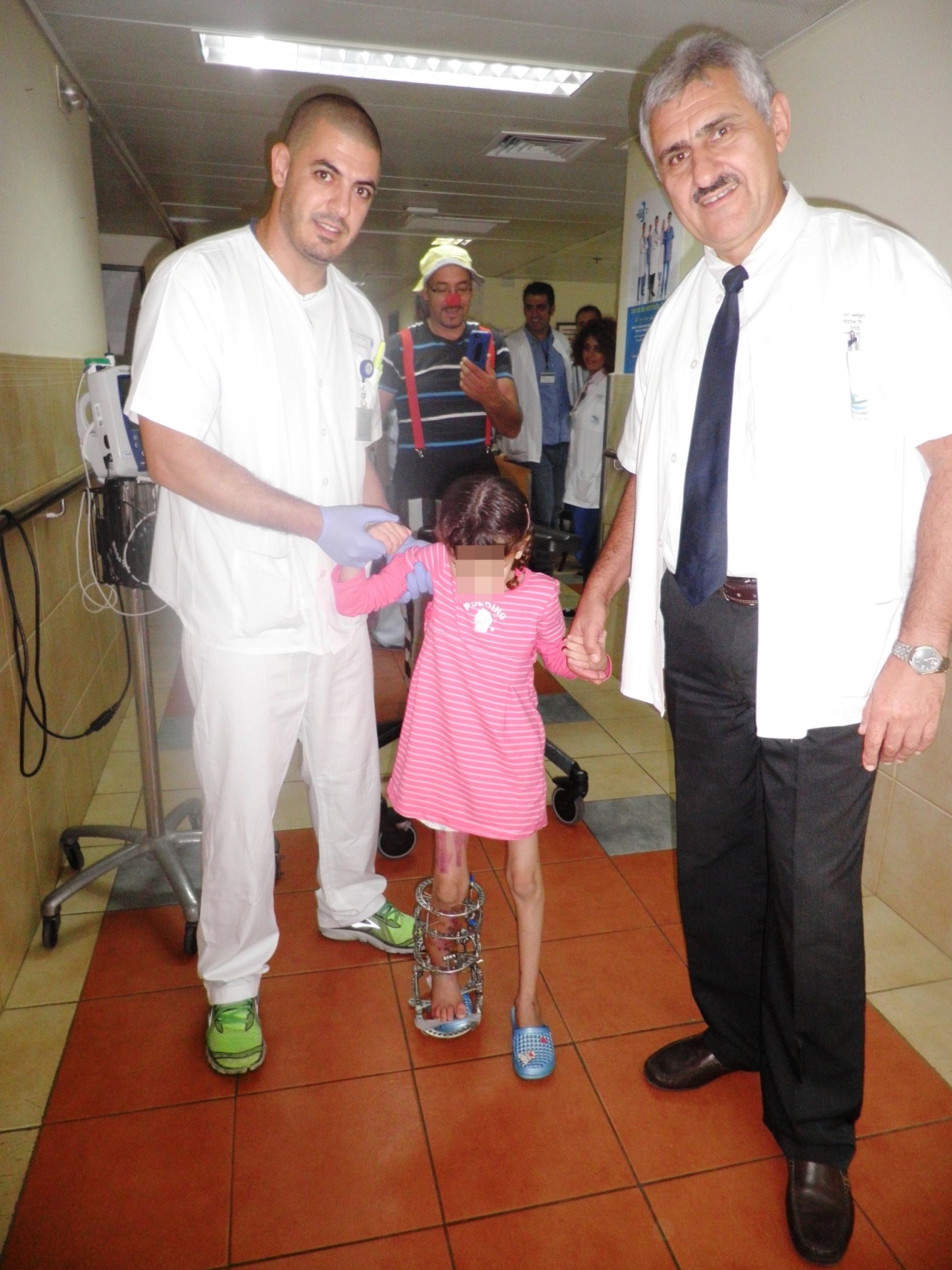 Dr Alexander Lerner, head of the Orthopedic department, and a nurse hold the hand of an eight-year-old Syrian girl whose legs were shattered by an explosion. This is the first time she is walking since the accident. Photo Ziv Medical Center